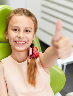 girl in dentist chair giving thumbs up after child dentistry